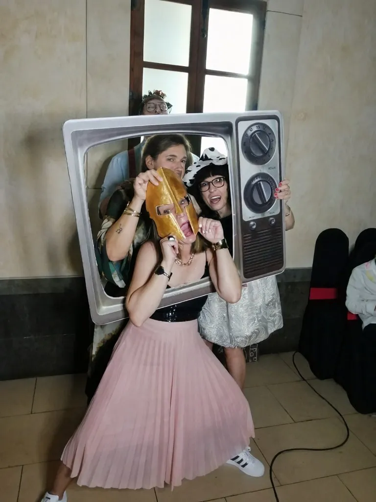 Amigas posando con un marco de televisión antigua, máscaras y diademas